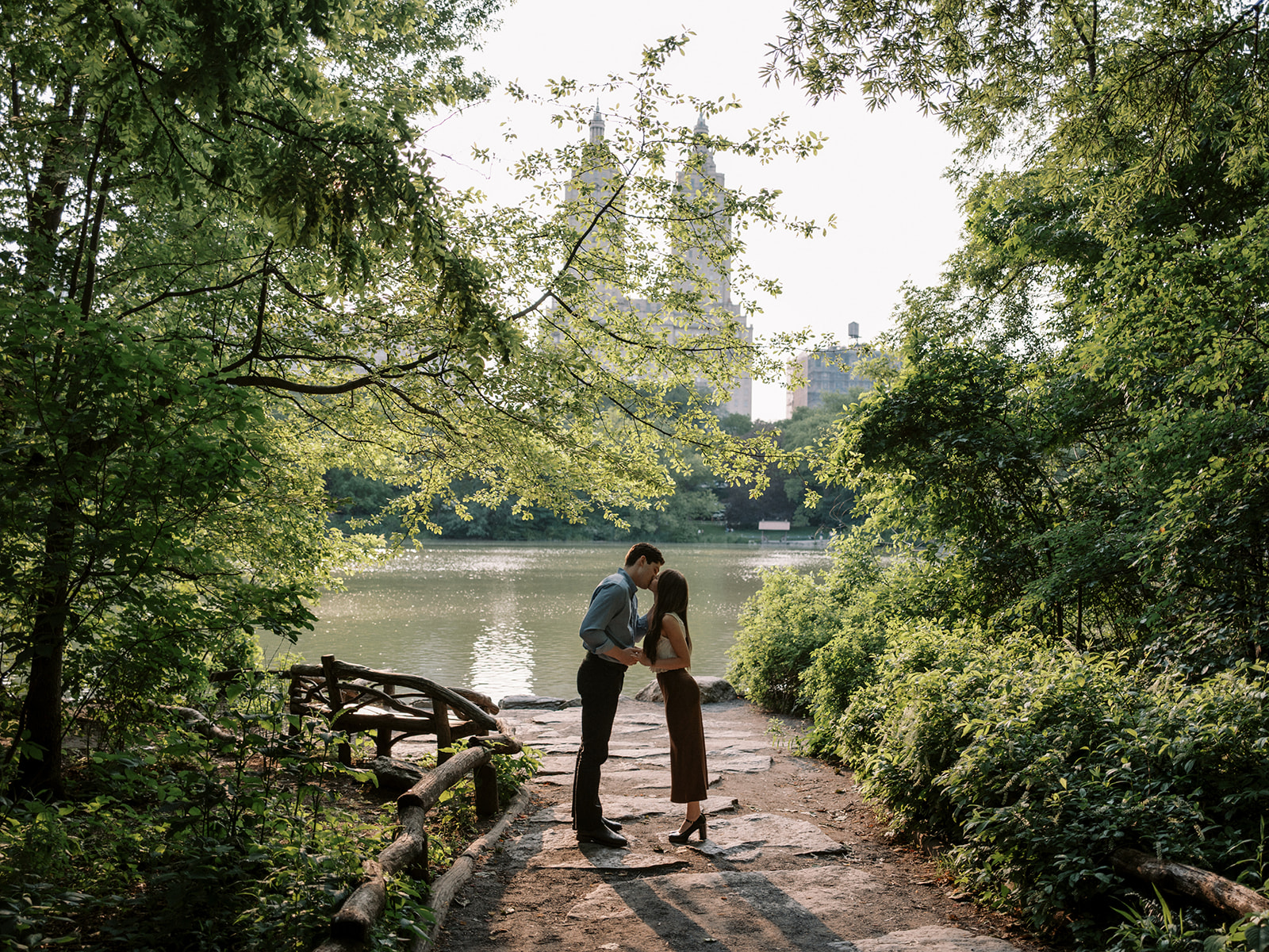 Romantic engagement session in Central Park NYC with a couple kissing near the lake at sunset