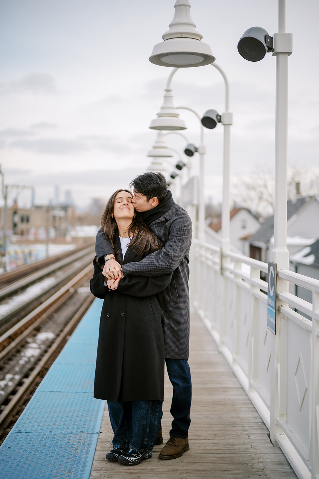 Couple embracing on a Chicago Blue Line train platform during their engagement session, candid city portrait