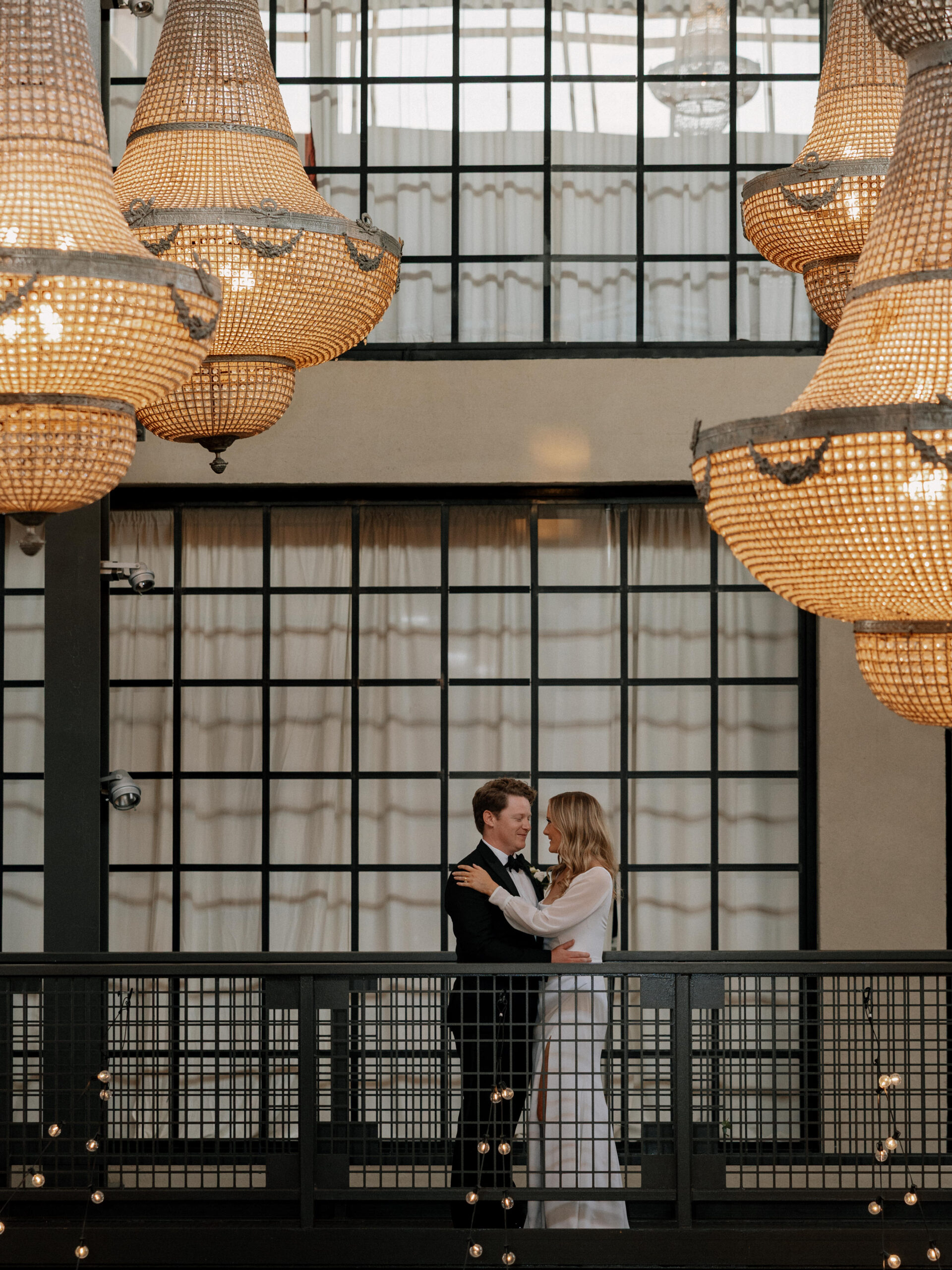 Bride and groom embracing on the balcony at Artifact Events in Chicago beneath warm chandelier lighting.