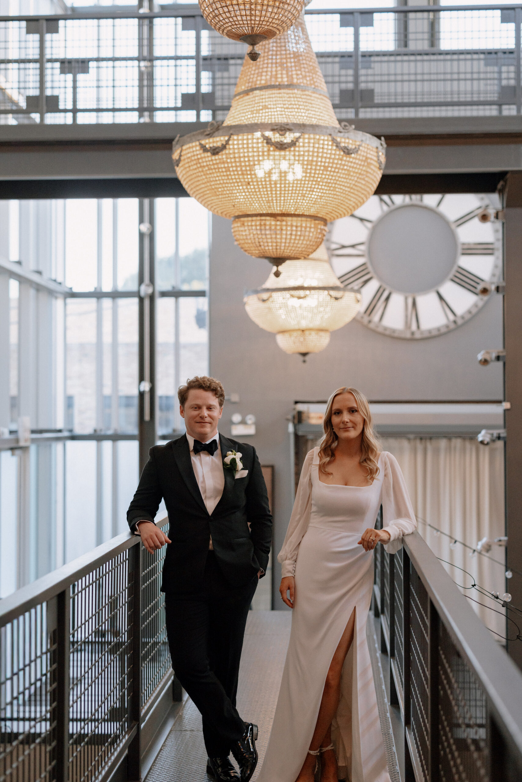 Bride and groom standing on the upper walkway at Artifact Events Chicago with industrial windows and chandeliers overhead.